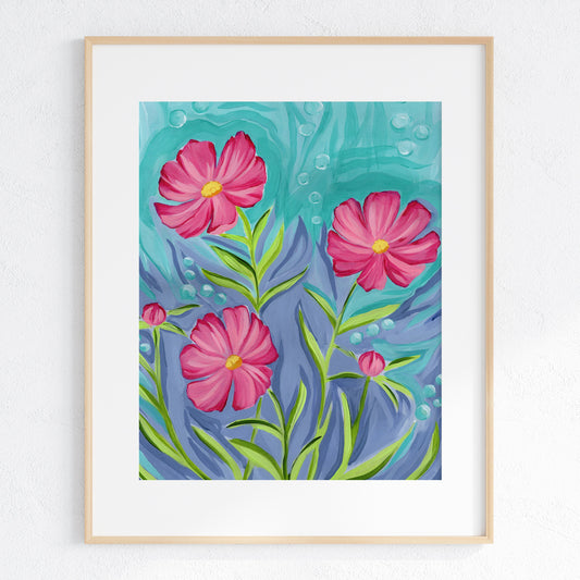 A framed art print featuring three pink cosmos flowers with green stems against a textured teal and blue background, displayed in a light wood frame on a white wall.